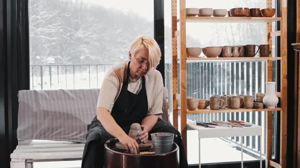 An Elderly Woman Potter Wetting Big Piece of Clay on the Wheel alt