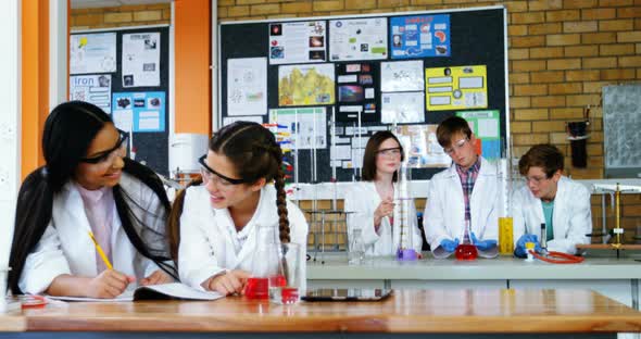 School girls writing in journal book while experimenting in laboratory at school alt
