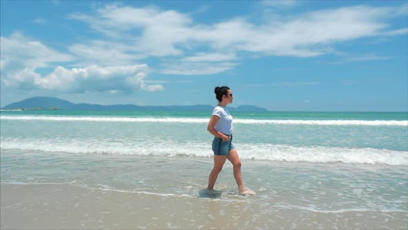 European Beautiful Brunette in Black Glasses, White-shirt and Blue Shorts Goes Under the Hot Summer alt