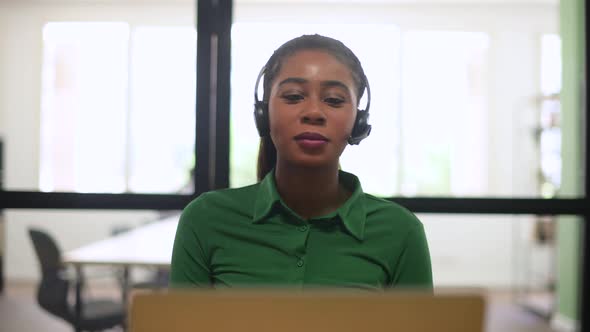 Smiling Africanamerican Female Employee Colleague Using Headset and Laptop Sitting on the Workplace