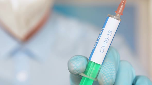 Close up of a researcher with face mask holding a syringe with coronavirus vaccine