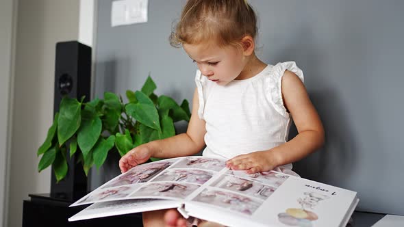 Happy Cute Little Girl Looking at Photos in Album alt