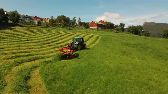 Aerial shot following a tractor cutting grass in a field in the mountains of Norway alt