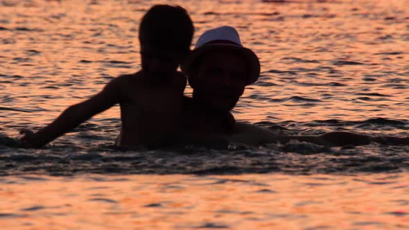 Parent and Son in the Sea with Sunset Reflecting in the Water. Family Tours, Trips. Travel To Europe