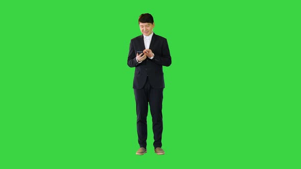 Asian Man in Suit Smiles While Using Mobile Phone on a Green Screen Chroma Key