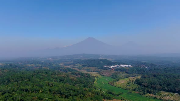 Grabag green valley with Sumbing and Sindoro mounts shrouded in fog in background. Aerial forward alt