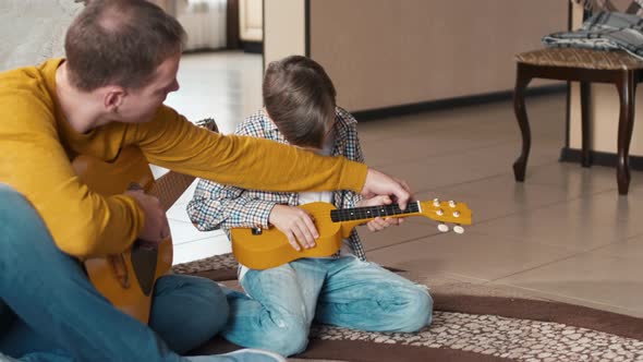 Caucasian man studying his son to play guitar