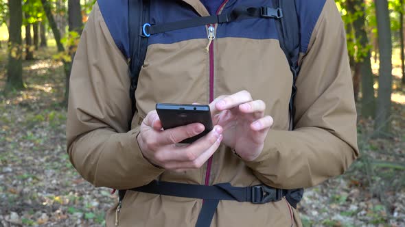 A Backpacker Works on a Smartphone in a Forest - Closeup alt
