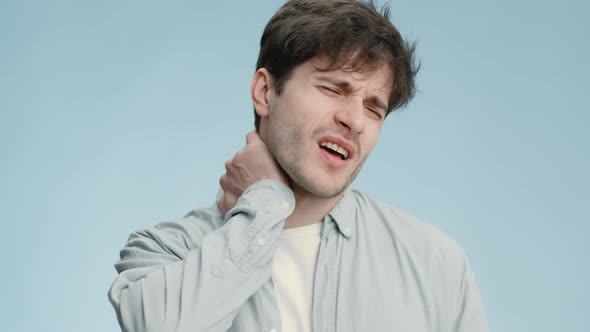 Studio Portrait of Young Sick Man Suffering From Neck Ache Massaging Painful Body Part and Grimacing alt
