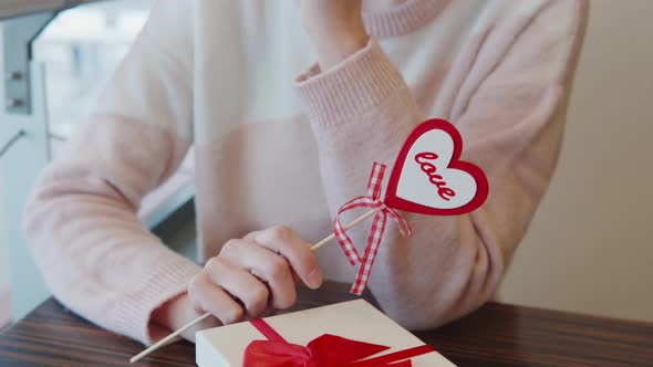 Nice Girl Holding Heart in Hand Near Saint Valentine's Day Present in Restaurant