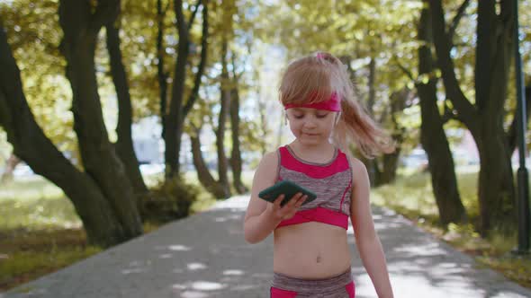Athletic Fitness Sport Runner Child Girl Walking Using Smartphone Listening Music with Earphones alt