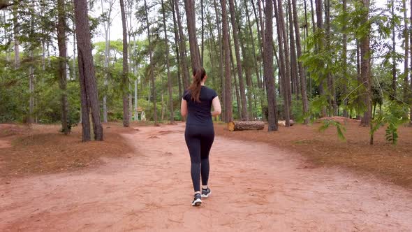 Girl running on a dirt trail between trees, cameraing from behing to the right side. alt