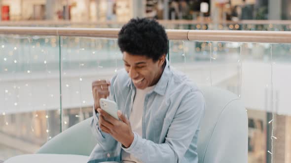 African Guy User Online Betting Mobile Game Win Sitting Indoors with Phone Success Yes Gesture Win alt