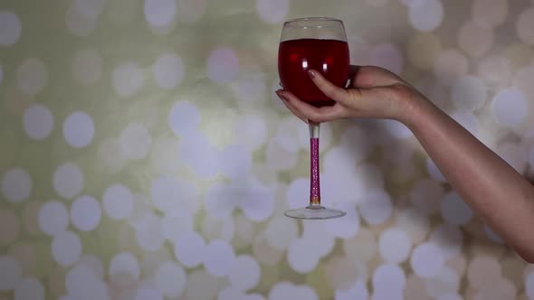 A woman's hand holding a glass of rose wine on a glittery background alt