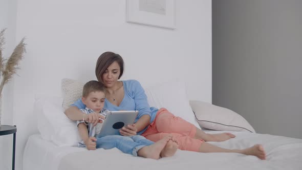 Mother and Son Using Digital Tablet in Bedroom at Home alt
