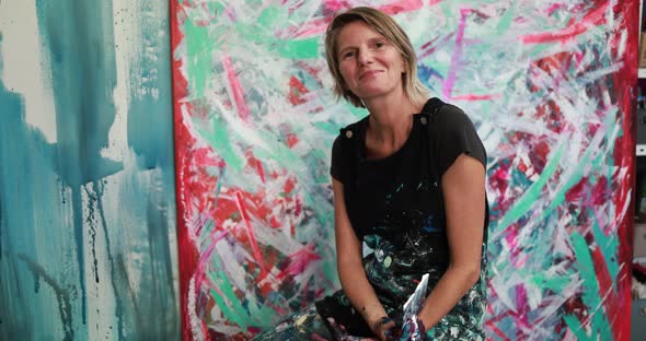 Happy senior woman after painting inside her atelier studio at home alt