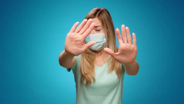 Young Woman in Medical Mask Stretching Out Hands Stop Gesture Against Blue Abckground alt