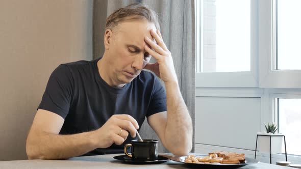 Adult Man in the Morning in the Kitchen, Thinking About Their Problems. He Is Drinking Coffee alt
