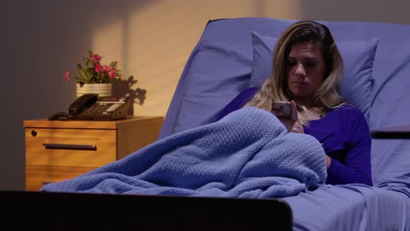 Woman in hospital bed at night using cell phone