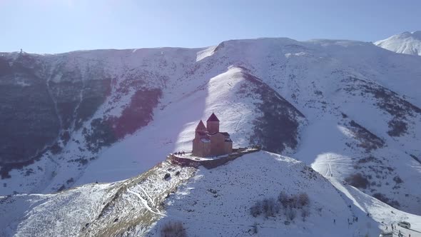 Aerial footage of lonely old medieval Gergeti Trinity Church in winter mountains in Kazbegi Georgia