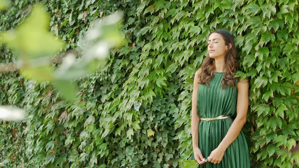 Woman in green summer dress leaning on overgrown wall
