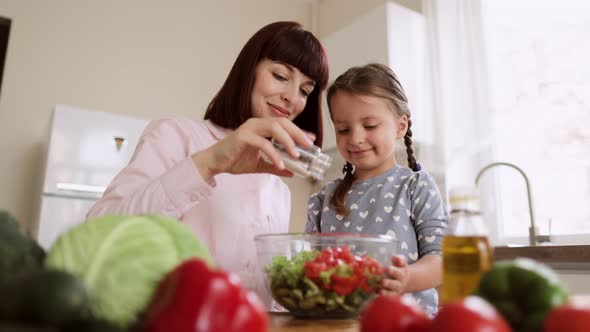 Portrait of Smiling Young Mom i and Little Daughter Adding Salt to the Salad While Cooking in alt