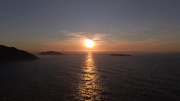 Fire sunrise over calm sea on coastal cliff horizon with orange hue reflection on the water. Mountai alt