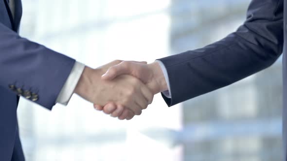 Close-up of Businessmen Shaking There Hands Against Boardroom Window alt