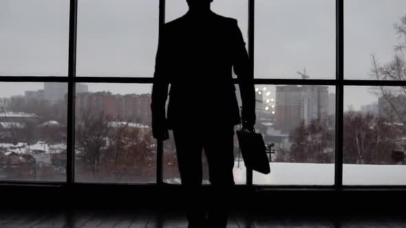 Businessman Approaches and Leans on the Window in the Office alt