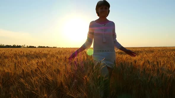 Young Attractive Brunette Walks Along a Wheat Field in White Dress at Sunset alt