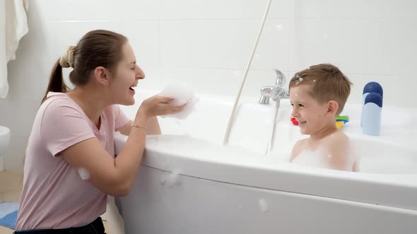 Happy Laughing and Smiling Mother with Son Playing in Bath with Soap Foam alt