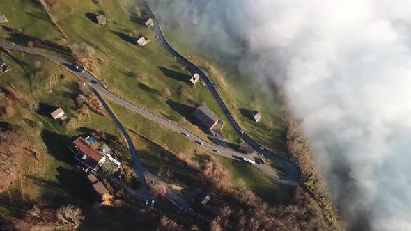 Curvy roads lead through small village on a mountain range with low clouds of fog in the valley. Top alt