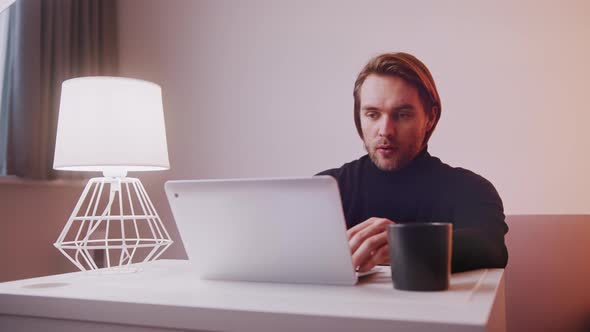 Caucasian Man Using Laptop at Home with Cup of Coffee Nearby alt