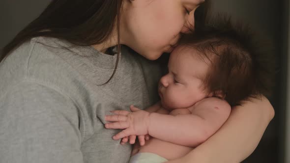 Authentic young mother holding newborn baby in her arms  kissing in head, lulls to sleep alt