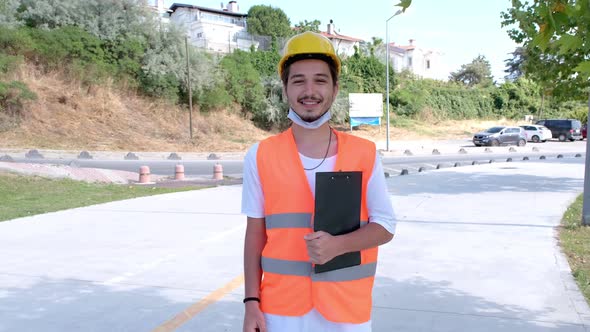 Portrait of young construction worker with white hardhat and face mask at construction site. alt