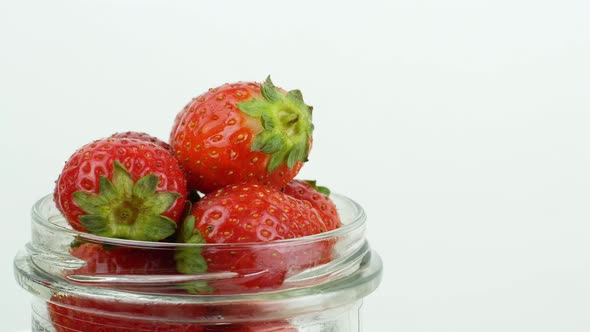 Glass jar with red ripe strawberries rotating on a white background. Ripe summer red strawberry