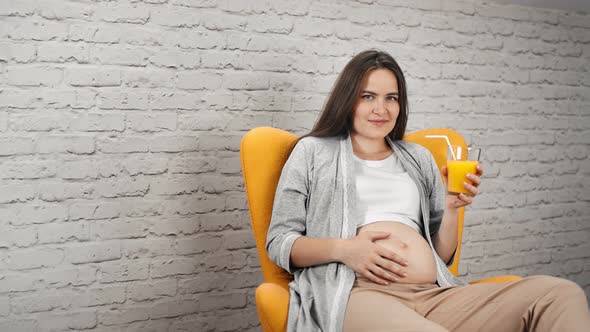 Charming Young Pregnant Girl Touching Naked Belly Holding Glass with Refreshing Vitamin Orange Juice alt