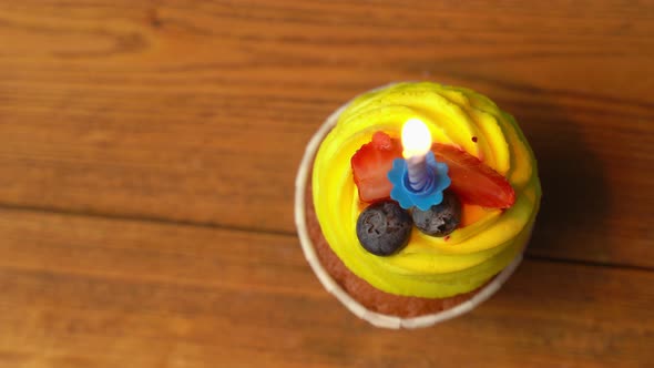 Top View of a Festive Cupcake with Yellow Cream with a Burning Candle Rotating on a Light Pink alt