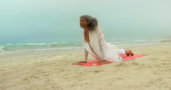 Front view of active senior African American woman doing yoga on exercise mat at the beach 4k alt