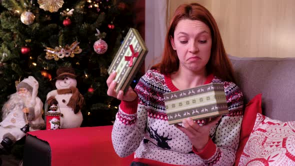 Sad Woman Lying on a Sofa Near the Christmas Tree, Opening Gift Disappointed and Unhappy alt