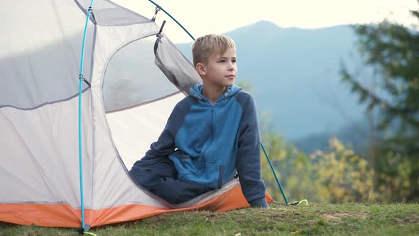 Hiker child boy sitting inside a tent in mountain campsite enjoying view of nature. alt