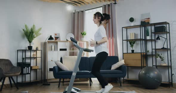 Woman Jogging on Treadmill at Home and Checking Indicators on Her smartwatch alt