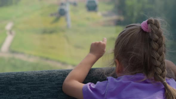 Blonde Girl with Plait Points Forward From Ropeway Cabin alt