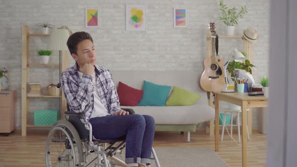 Sad Young Asian Man Disabled in a Wheelchair in the Living Room alt