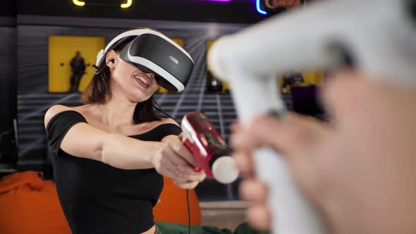 Man and Woman Use a Virtual Reality Headset with Glasses and Hand Motion Controllers and Weapons