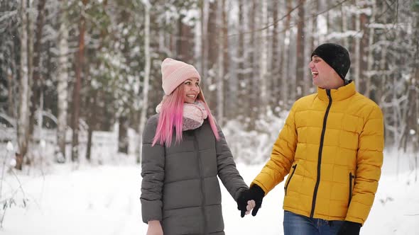 A Man in a Yellow Jacket and a Girl in a Hat and Scarf Walk Through the Winter Forest During a alt