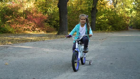 Little girl riding four wheeled bicycle in park alt