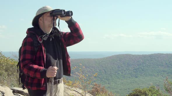An older hiker looking through binoculars while on a scenic hike in the mountains. alt