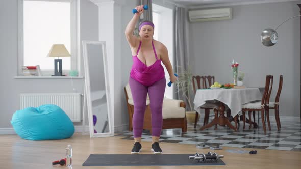 Persistent Serious Motivated Obese Woman Lifting Dumbbells Training at Home Indoors alt
