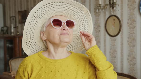 Playful and Pretty Senior Caucasian Woman with Pink Sunglasses and a Hat Smiling Happily Medium alt
